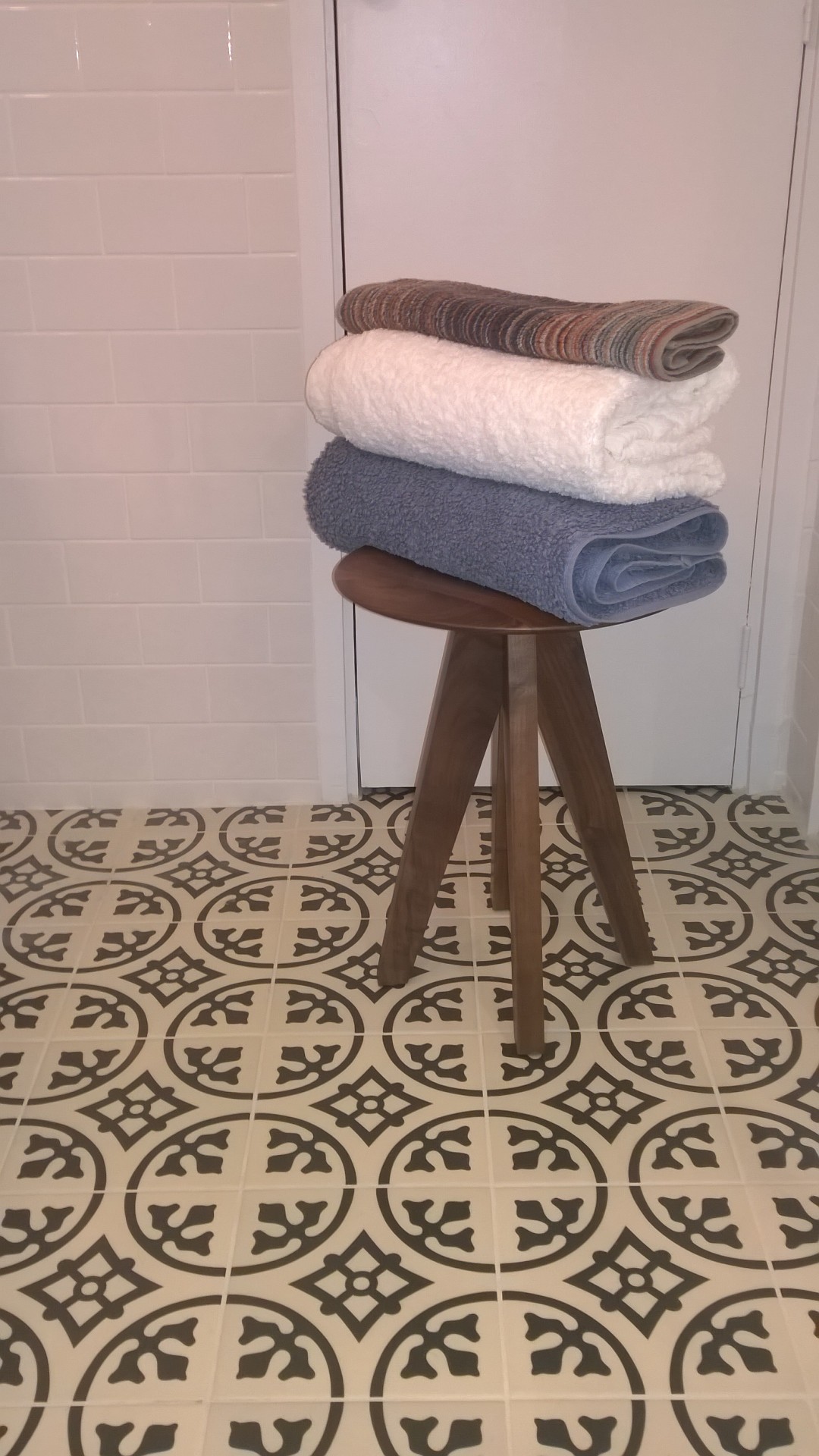 Wooden stool with folded towels on a floor with patterened floor tiles